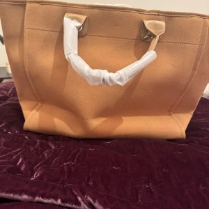 Light light brun  shopping/beach väska med kedjehandtag - Stilren shopping/strand väska i beige/ljus brun bomullstyg med rejäla handtag i silverfärgad kedja. Robust väska som klarar massa saker i den. Väskan har en rymlig insida med flera fack och magnetknäppning upptill. Perfekt för dig som vill ha plats för allt och ändå se chic ut. Riktigt bra väska att ha till allt. Skickar direkt vid betalning. Så köpare får sin vara snabbt och kan använda den.  Då jag själv gillar allt jag säljer. 