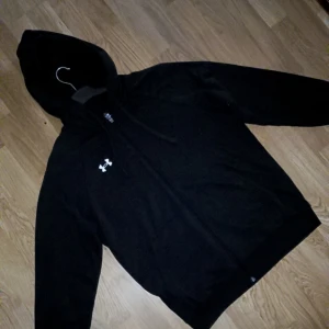 Svart hoodie från Under Armour riktigt fin - Svart hoodie från Under Armour med dragkedja och huva. Tröjan har snörning vid huvan, lång ärm och en vit logga på bröstet. Tillverkad i mjuk polyester, perfekt för träning eller chill. Snygg och enkel design som funkar året runt. Använd 3 ggr max som NY ! ST SMAL men kan passa medium  köptes för 1000 säljer för 600 och mjukisen e helt nya bara testade st S passar M oxå pris 500 säljer båda för 800