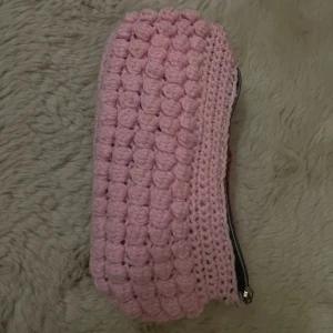 Stickad rosa väska - Supergullig handgjord väska design av bubblig struktur. Det går bra att användas som plånbok men också väska för pennor. Ena sidan är ljusrosa och andra sidan mörkare röd, med en praktisk dragkedja upptill. Perfekt för pennor, smink eller småprylar. Unik accessoar som sticker ut i väskan!
