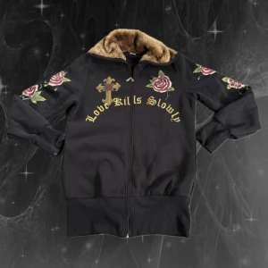Svart hoodie Ed Hardy  - Svart hoodie från Ed Hardy med bruna fuskpälsdetaljer i kragen. Hoodien har rosor och kors på både fram- och baksida samt texten 'Love Kills Slowly'. Dragkedja framtill och Ed Hardy-logga bak. Materialet är 100% bomull. Skulle säga mer L än XXL.