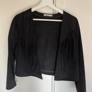 Svart kofta/jacka med fransar  - Svart ”jacka” i mocka med fransar. Den kommer från Gina tricot och är i strl S. Mycket bra skick!
