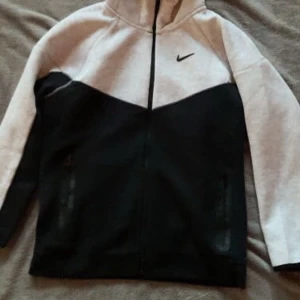 Nike nocta svart och grå - Nike hoodiejacka i svart och ljusgrått med dragkedja framtill och huva. Jackan har två fickor med dragkedja och en stilren design med Nike-logga på bröstet. Perfekt för en sportig och avslappnad look.  Storlek XL men sitter som M/L 