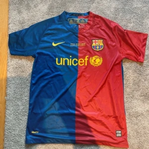 Barcelona Final Roma 2009 fotbollströja - Säljer en officiell FC Barcelona matchtröja från Final Roma 2009, tillverkad av Nike i Dri-FIT material. Tröjan har korta ärmar och är delad i blått och rött med gula detaljer, klubbmärke och UNICEF-logga på bröstet. Perfekt för dig som älskar Barca!