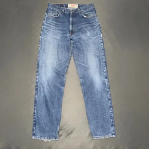 Levi's 501 blå jeans straight fit - Klassiska Levi's 501 jeans i blå tvätt med raka ben och fem fickor. Jeansen har normal passform, knappgylf och slitna kanter vid bensluten för en cool vintagekänsla. Perfekta för dig som gillar tidlös denimstil.