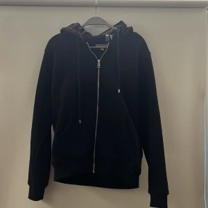 Svart Burberry hoodie med rutig huva - Säljer nu min riktigt snygga svarta burberry hoodie i storlek S och är använd typ en gång, och passar dig som e från 170-180cm ungefär skulle jag säga, en extremt bekväm och varm hoodie för ett bra pris, påsen på bilden skickas även med, för frågor är det bara att komma privat😁