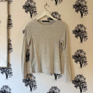 Ljusgrå långärmad tröja lager 157 - En enkel och stilren ljusgrå långärmad tröja från 157. Tröjan har rund halsringning och är gjord i mjuk bomullsmix som känns skön mot huden. Perfekt att matcha med jeans eller under en jacka. Passformen är normal och materialet är tunt och smidigt.