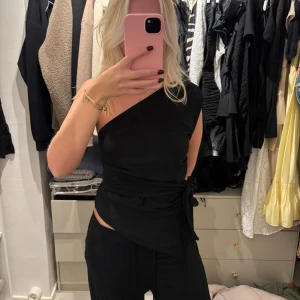 Svart oneshoulder topp med knyt - Säljer en svart oneshoulder topp med snygg knytning i midjan. Nästan nytt skick 