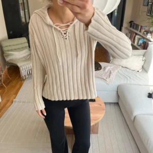 Beige stickad hoodie från Flashlights - Säljer en beige stickad hoodie från Flashlights i storlek 40/42. Tröjan har ribbad struktur, snörning vid halsen och huva. Långärmad och i mjukt bomullsmaterial, perfekt för dig som gillar chill och snygg stil.