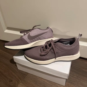 Nike dualTone Racer woman - Nike dualTone racer sneakers i en snygg lila ton med stickad mesh-överdel och klassisk swoosh på sidan.  Oanvända skor då jag tyvärr inte hann  använda dom innan graviditet och nu efter graviditeterna så passar dom inte. Kartong finns tyvärr inte, inköpt på JD sport.