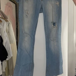 Low bootcut ljusblå jeans - Super snygga lowrise bootcut jeans men slitningar. Säljs pågrund av att de passar inte längre. En liten färgfläck på baksidan men den syns inte om man har på sig dem eller tvättar med något speciellt som kan ta bort det. Köpt ifrån vinted och använd fåtal gånger. Skriv för frågor