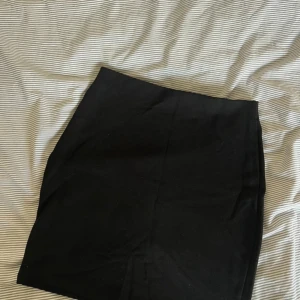 Svart enkel kortkjol - Säljer en svart, stilren kortkjol med rak passform. Kjolen är enfärgad och har en klassisk look som är lätt att matcha med olika toppar. Perfekt för dig som gillar minimalistisk stil och vill ha en basic kjol i garderoben.