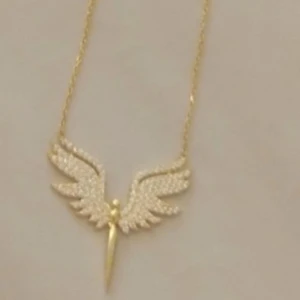 Guldigt halsband med änglavingar 925 sterling silver  - Unikt halsband i guld med ett hängsmycke som föreställer änglavingar och en stiliserad figur. Vingarna är dekorerade med små glittriga detaljer som ger extra shine. Perfekt för dig som gillar statement-smycken med cool design.