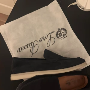 Mörkblå mockaloafers från Loro Piana - Snygga mörkblå loafers från Loro Piana i mjuk mocka med vit platt sula. Skorna har en klassisk och stilren design med rund tå och diskreta sömmar. Perfekta för dig som gillar en clean och exklusiv look.