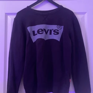 Svart sweatshirt från Levi's - Svart sweatshirt från Levi's med klassiskt stort logotryck i grått framtill. Tröjan har rund halsringning och långa ärmar, perfekt för en chill och stilren look. Mjuk och skön, passar till allt. 