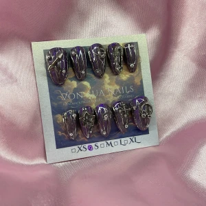 PurpleY2K (S);Short Almond;Curved - Handgjorda press-on naglar i lila med glitter och coola silverdetaljer som stjärnor, kors och ringar. Naglarna har en kort almond form och metallic finish, perfekta för dig som vill sticka ut med din nagelstil.S: 15 mm, 11,5 mm, 12 mm, 11 mm, 9 mm 