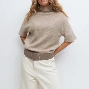 Beige polotröja från Gina - Säljer en stilren beige polotröja med korta ärmar och hög hals. Tröjan är i mjuk ullblandning och har en avslappnad passform som är perfekt för lager-på-lager. Enkel att matcha med både jeans och kjol för en clean look aldrig använt ❤️