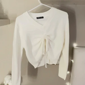 Vit stickad tröja med snörning  - Vit stickad tröja från SHEIN med v-ringad hals och snygg snörning framtill som ger en cool, croppad look. Långärmad och mjuk i materialet, perfekt för dig som gillar stilrena och trendiga detaljer. Passar dig som vill ha en enkel men ändå unik tröja.