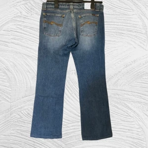 Nudie Jeans BootCutOla - Snygga Nudie Jeans Bootcut i klassisk blå denim 💙 Lätt utsvängda ben och croppad fit (kapade till ca 97 cm) – perfekt över sneakers eller boots 👟 Ger en ren Y2K / retro look med den där äkta vintagekänslan. I fint skick, inga hål – bara naturlig fading och perfekt passform.