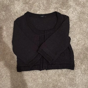 Svart kofta - Svart  kofta från Cropp med grovstickad struktur och ribbade detaljer vid hals, knappkant och nederkant. Koftan har trekvartsärm och två dekorativa fickor framtill. Perfekt för lager-på-lager och chill stil.