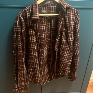 Brun rutig skjorta från Dressmann - Snygg brun skjorta med vitt rutmönster från Dressmann. Skjortan har klassisk krage, långa ärmar och knappar framtill. Perfekt för dig som gillar en avslappnad men stilren look. Materialet känns mjukt och bekvämt mot huden. Perfekt som overshirt eller på en cowboy fest. Original pris 500