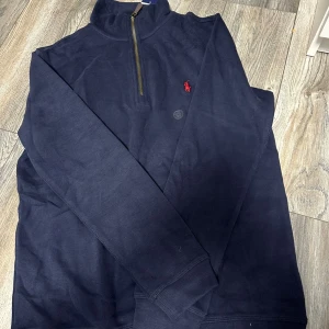 Marinblå half zip tröja Polo Ralph Lauren - Snygg marinblå långärmad tröja från Polo Ralph Lauren med half zip och klassisk röd broderad logga på bröstet. Tröjan är i mjuk bomull och har en ribbad krage och muddar. Perfekt för dig som gillar stilrena och sportiga plagg.