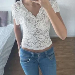 Spets topp - Supersöt vit blus i spets från designbysi med korta ärmar och v-ringad hals. Blusen har ett blommigt spetsmönster. perfekt till jeans eller kjol. Onsize.