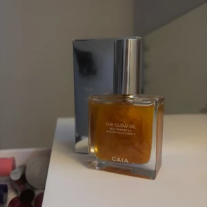 CAIA The Glow Oil Shimmer - The Glow Oil från CAIA är en lyxig kroppsolja med guldigt skimmer, berikad med avokadoolja och vitamin E. Kommer i en snygg fyrkantig glasflaska med silvrig kork. Perfekt för att ge huden en glowy finish.