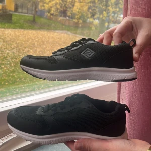 Svarta sneakers med vit sula - Svarta sneakers med vit, mönstrad sula och snörning. Ovandelen är i mesh och syntet med en stilren logga på sidan. Skorna har rund tå och platt sula, perfekta för en sportig look eller till vardagsoutfiten.