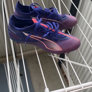 Puma Ultra blå/lila fotbollsskor - Säljer ett par Puma Ultra fotbollsskor i blå och lila med röda detaljer. Skorna har snörning, platt sula med dobbar och är tillverkade i lätt syntetmaterial. Perfekta för dig som vill sticka ut på planen med snygg design och grym passform.