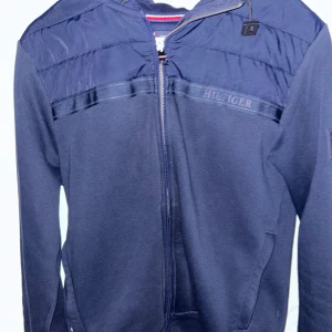 Tommy Hilfiger Cardigan/jacka - Snygg mörkblå Jacka/Cardigan från Tommy Hilfiger med dragkedja framtill, även huva. Det är en logga på bröstet och ärmen. Perfekt nu till hösten och vintern för dig som gillar stilren och klassisk streetwear! 🙌🏽Det finns inga synliga defekter förutom att den är använd, nypris: 2200kr