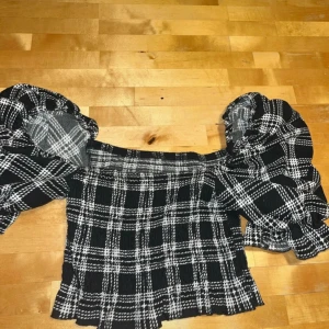 Svartvit rutig blus från Bik Bok - Säljer en svartvit rutig blus från Bik Bok i storlek XS. Toppen har puffiga offshoulder-ärmar och är croppad med volangkant nedtill. Materialet är mjukt och stretchigt, perfekt för dig som gillar statement-plagg med coola detaljer.