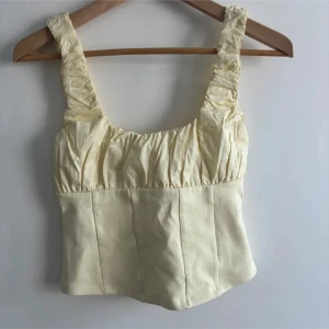 Ljusgul croppad linnetopp med rynk - Säljer en ljusgul croppad linnetopp med breda axelband och snygga rynkdetaljer upptill. Toppen har en fyrkantig halsringning och är tillverkad i ett mjukt material som känns skönt mot huden. Perfekt för varma dagar och sommarhäng!