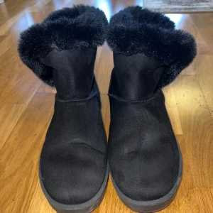 Svarta boots från Esmara - Mysiga svarta boots från Esmara i storlek 41. Skorna har en fluffig fuskpäls runt skaftet och är tillverkade i syntetmaterial med en platt sula. Perfekta för kalla dagar när du vill hålla fötterna varma och ändå se snygg ut.