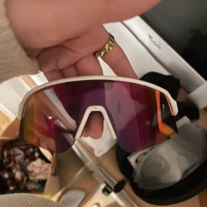 Oakley vita sportglasögon - Säljer ett par feta Oakley sportglasögon med vit ram och stora, spegelblanka linser i lila och orange ton. Modellen har en futuristisk sköldform och Oakleys logga på sidan. Perfekta för cykling eller träning utomhus. Helt oanvända enbart testad, säljer då de inte var min stil av glasögon. Köpta för 2200 och aldrig använda utan. Tillkommer extra glass och plus en låda med dragkedja som man kan stäng. Och skyddspåse som man sätta de i.💗💗