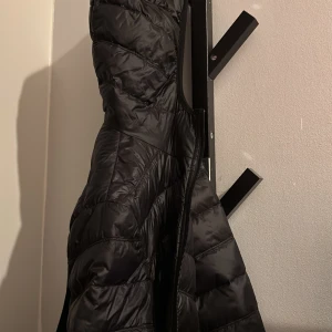 Svart pufferjacka med dragkedja - Säljer en svart pufferjacka med snygg quiltad design och hel dragkedja framtill. Jackan är vadderad och perfekt för kyliga dagar. Passar dig som gillar en stilren och sportig look.