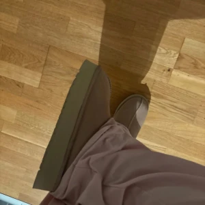 Beige UGG platå boots - Säljer ett par beige UGG boots med platåsula och rund tå. Skorna är i mjuk mocka med stickad detalj runt öppningen och har en rejäl, räfflad sula för extra grepp. Perfekta för kalla dagar och riktigt sköna att ha på sig.