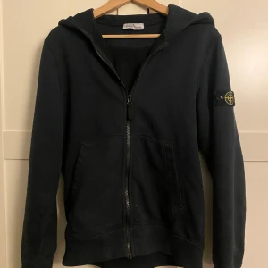 Stone island zip hoodie - Säljer en stilren mörkblå stone island hoodie med zip i storlek 14y/170, passar ca 170-180/S. Jag är 177 och den funkar fortfarande på mig men börjar bli lite liten. Köpt på nk och nypris är ca 2000kr. Tröjan är i gott skick och sparsamt använd utan fläckar elr slitage. Man tvättar tröjan utan kompasspatchen som är väldigt enkel att ta av. Det kommer även till en extra knapp vid lapparna på insidan. Hör av dig om du har några frågor elr liknande🙌