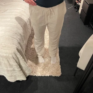 Beiga linnebyxor med snörning - Snygga och sköna beiga linnebyxor med snörning i midjan. Byxorna har en avslappnad passform och är perfekta för chill dagar. Materialet är linne och de har elastisk midja för extra komfort.