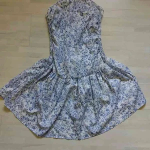 Vit och blå blommig kortklänning - Supersöt axelbandslös kortklänning i vitt med blått blommönster. Lätt och luftig vid kjol-delen. ribbad vid ryggen så den åker inte ner. aldrig använd.