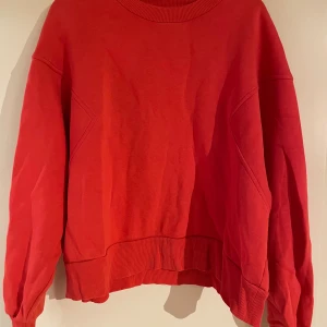 Röd sweatshirt från Gina Tricot - En röd oversized sweatshirt från Gina Tricot i storlek L. Tröjan har ribbade muddar vid hals, ärmslut och nederkant samt en klassisk rund halsringning. Tillverkad i mjuk bomullsmix, perfekt för chill dagar och enkel att styla med jeans eller leggings.