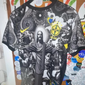 Brasil Nike fotbollströja svart/gul - Unik Brasilien fotbollströja från Nike med coolt svart och vitt grafiskt tryck på framsidan, inklusive Kristusstatyn och Brasil-logga i gult. Kortärmad och tillverkad i lätt, ventilerande Dri-FIT material. Snygga detaljer och kontrasterande färger som sticker ut.