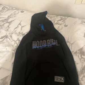 Hoodrich - Svart hoodie från Hoodrich i storlek S med blå insida på huvan och blått tryck på bröstet.