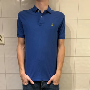 Blå pikétröja från Polo Ralph Lauren - Klassisk blå pikétröja från Polo Ralph Lauren i jätte bra skick! Jag på bilden är 184cm lång och väger 70kg. Hör av er vid frågor eller funderingar!👌✌️