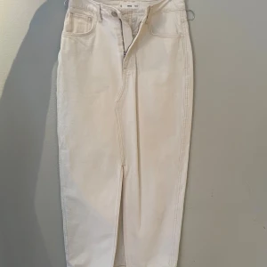 Vit lång jeanskjol från Mango - Säljer en vit lång jeanskjol från Mango med klassisk femficksdesign, hög midja och slits framtill. Kjolen har bälteshällor och dragkedja med knapp. Perfekt för dig som gillar stilren och enkel denim.