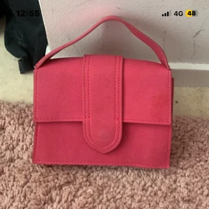 Rosa mocka axelväska med handtag - Snygg fyrkantig axelväska i rosa mocka med matchande handtag och avtagbar axelrem. Väskan har stilren design med lock och magnetstängning. Perfekt storlek för mobil, plånbok och småsaker. Guldiga detaljer på axelremmen ger en extra touch.