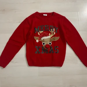 Röd jultröja med renmotiv och paljetter - Röd stickad jultröja från Kappahl med ett stort renmotiv framtill, paljetter i grönt och guld samt en mjuk röd nos. Texten 'Merry Xmas' i paljetter och detaljer som tomteluva och broderade horn. Perfekt för julens alla tillfällen! Storlek 158/164 eller XS. Hör av dig vid frågor och priset kan diskuteras!💕