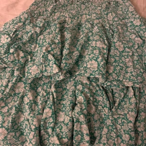 Grönblommig volangklänning - Supersöt kort klänning med grönt och vitt blommönster och volanger. Smockad upptill för en bekväm passform och luftig kjol. Perfekt för dig som gillar romantisk och somrig stil. Från Samsa i storlek S