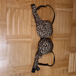 Leopardmönstrad och svart Triple Boost BH - Snygg BH med leopardmönstrad framsida och svart baksida. Kuporna är vadderade och har en boost-effekt. Axelbanden är justerbara och kanten har en liten spetsdetalj. Materialet är nylon, polyester och elastan. Perfekt för dig som vill ha lite extra push.