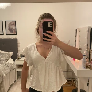 Vit blus med volang från 157 - Säljer en vit blus från 157 i storlek M. Blusen har v-ringad hals, korta volangärmar och en luftig, lätt struktur.