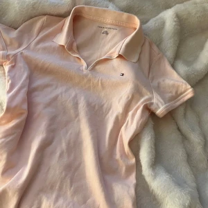 Ljusrosa pikétröja Tommy Hilfiger - Snygg ljusrosa pikétröja från Tommy Hilfiger med klassisk krage och korta ärmar. Tröjan har ett litet broderat logomärke på bröstet och är gjord i mjuk bomull. Perfekt för dig som gillar stilrena och fräscha plagg med en sportig touch.